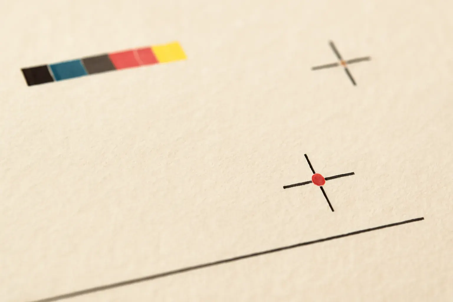 Close-up texture of a cream press-proof sheet showing registration marks, a crop-mark tick and a small printed colour bar.